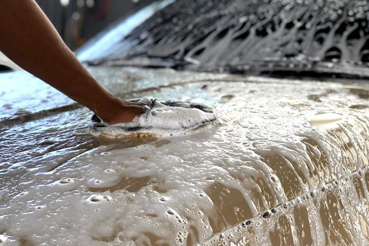 A wash mitt moving through thick foam on a car hood