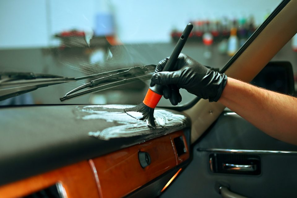 A gloved hand cleaning a car dashboard with a detailing brush