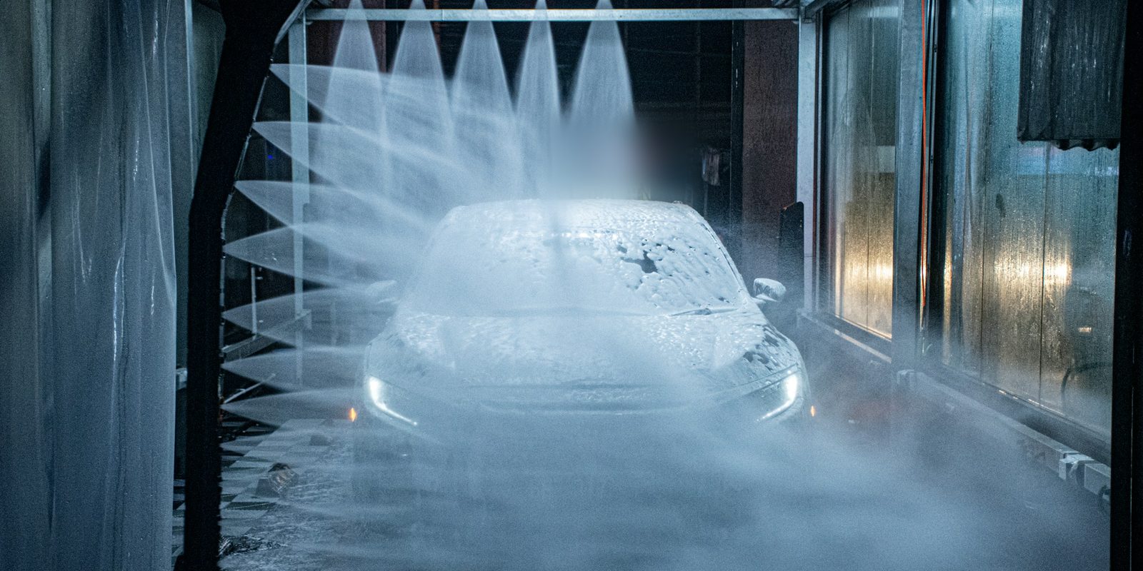 Water jets spraying a foam-covered car inside an automatic car wash
